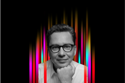 On the middle of a black background is a row of colourful vertical stripes’. In the centre is a black and white profile photo of TEDx speaker Sergey Young superimposed on top.